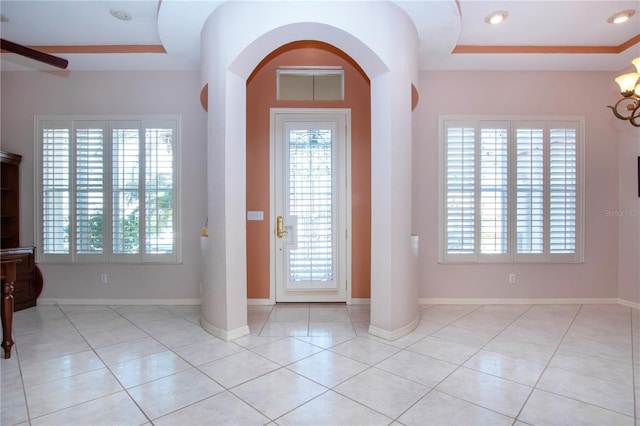 tiled foyer featuring baseboards, a raised ceiling, and a healthy amount of sunlight