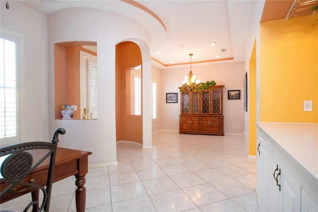 entryway with arched walkways, a notable chandelier, light tile patterned floors, a raised ceiling, and baseboards