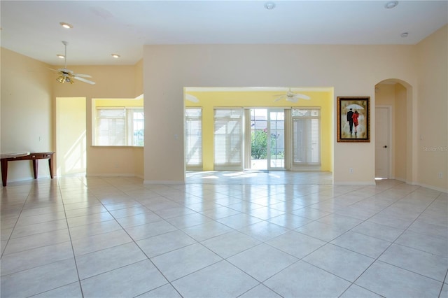 unfurnished room with arched walkways, light tile patterned flooring, baseboards, and a healthy amount of sunlight