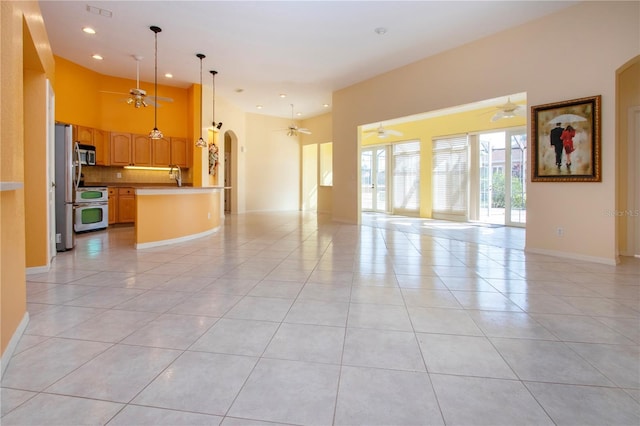 unfurnished living room with light tile patterned floors, ceiling fan, and arched walkways