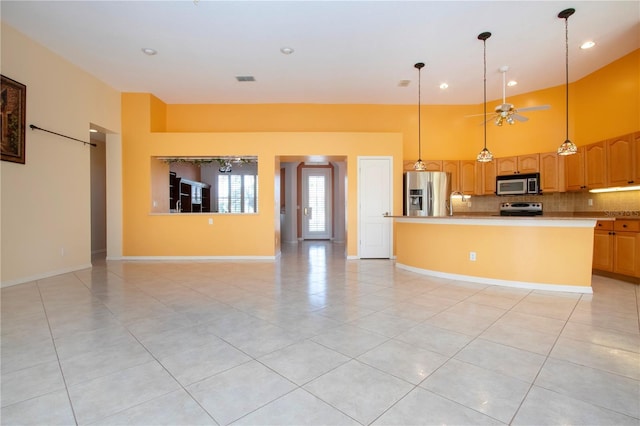 kitchen featuring a center island with sink, decorative backsplash, a towering ceiling, ceiling fan, and appliances with stainless steel finishes