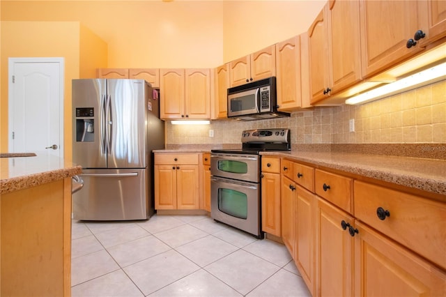 kitchen with light tile patterned floors, stainless steel appliances, backsplash, light stone countertops, and light brown cabinetry