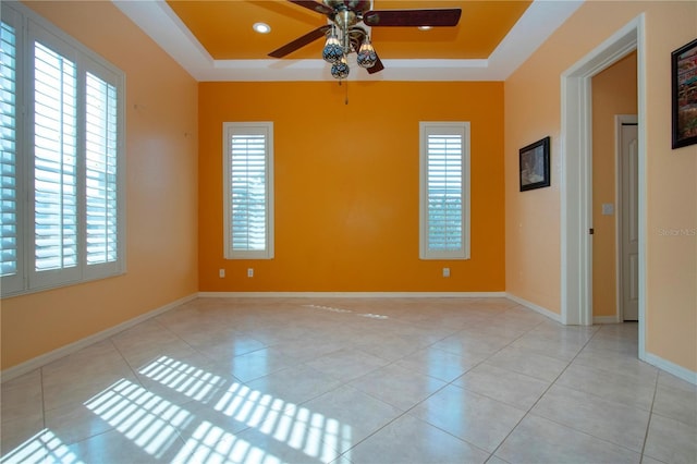 empty room with a ceiling fan, a raised ceiling, baseboards, and tile patterned floors