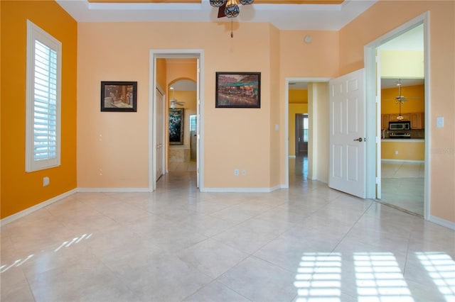 empty room with ceiling fan, light tile patterned flooring, arched walkways, and baseboards