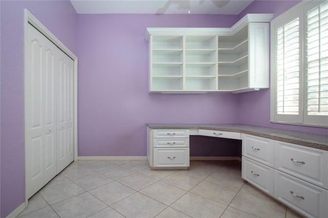 unfurnished office with light tile patterned floors, a ceiling fan, baseboards, and built in desk