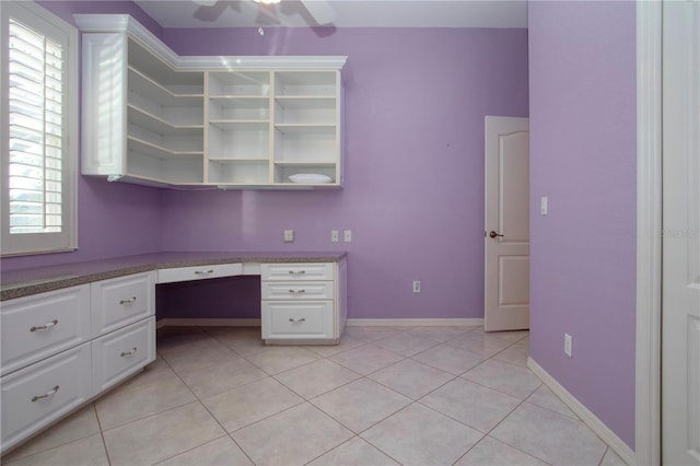 unfurnished office featuring a healthy amount of sunlight, light tile patterned floors, baseboards, and built in desk