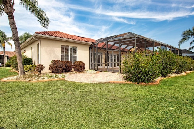 rear view of house featuring a yard, stucco siding, a patio area, a lanai, and a tiled roof