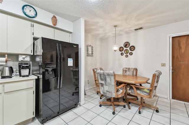 kitchen featuring light tile patterned flooring, a textured ceiling, white cabinets, black fridge with ice dispenser, and decorative light fixtures