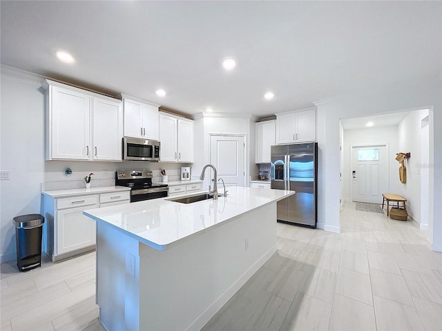 kitchen with sink, crown molding, appliances with stainless steel finishes, white cabinetry, and an island with sink