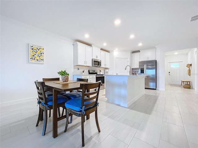 kitchen with stainless steel appliances, ornamental molding, a kitchen island with sink, and white cabinets