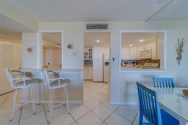 kitchen with a breakfast bar, backsplash, white cabinets, light tile patterned floors, and white appliances