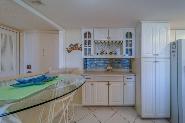 kitchen featuring white refrigerator, white cabinetry, light tile patterned flooring, and backsplash