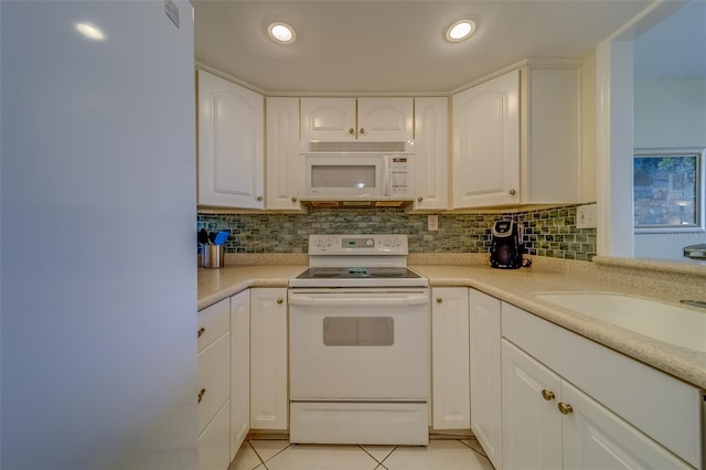 kitchen with light tile patterned floors, white appliances, white cabinets, and backsplash