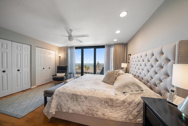 bedroom featuring two closets, expansive windows, hardwood / wood-style flooring, access to outside, and ceiling fan