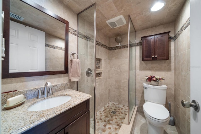 bathroom with vanity, a tile shower, tile walls, and toilet