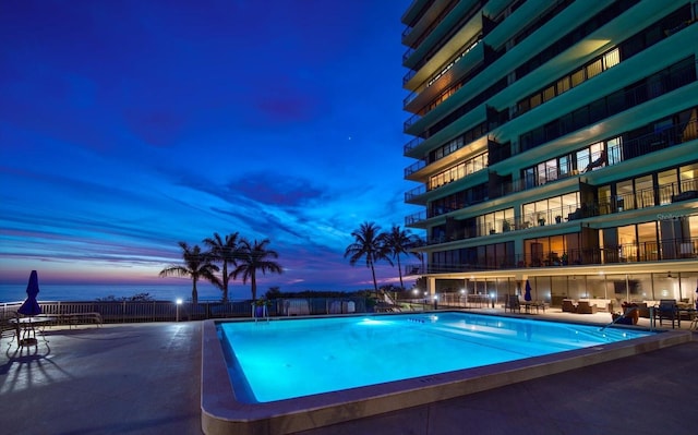 pool at dusk featuring a water view and a patio