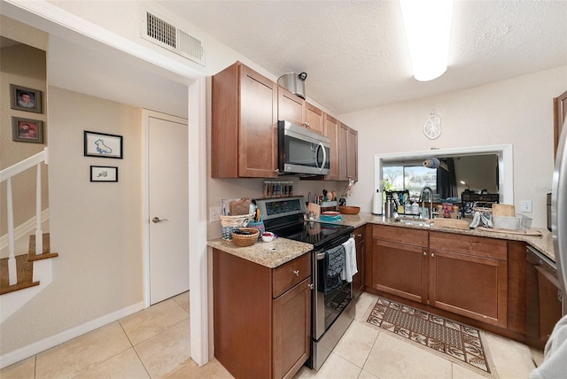 kitchen featuring light tile patterned flooring, appliances with stainless steel finishes, light stone counters, and a textured ceiling