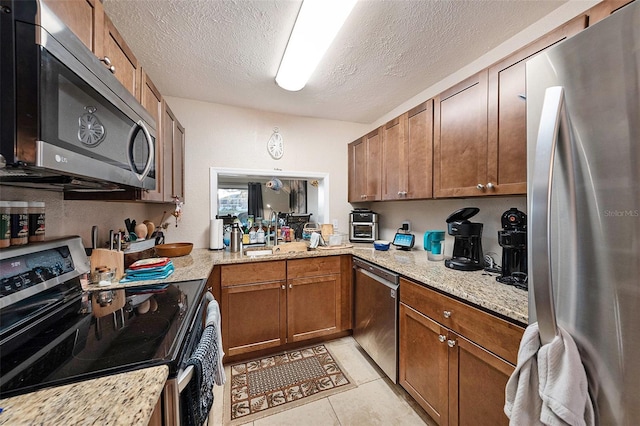 kitchen with stainless steel appliances, light stone countertops, a textured ceiling, and light tile patterned floors