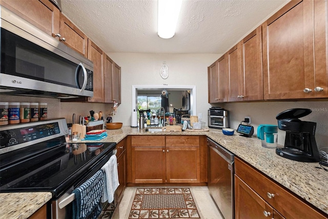 kitchen featuring light tile patterned flooring, sink, stainless steel appliances, light stone countertops, and a textured ceiling