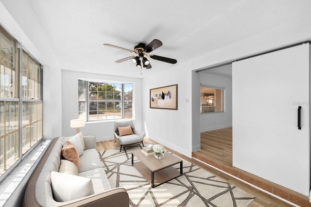 living room with light wood finished floors, ceiling fan, baseboards, and a textured ceiling