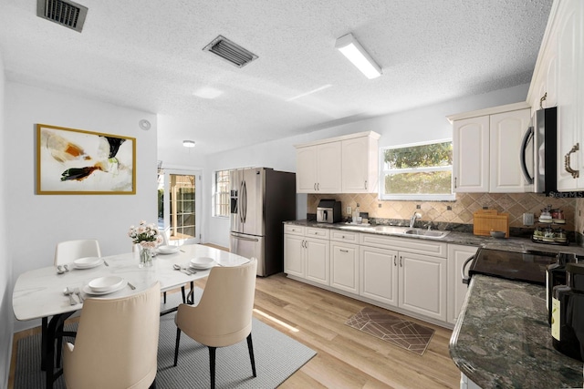 kitchen featuring visible vents, dark stone counters, light wood-style flooring, stainless steel appliances, and a sink