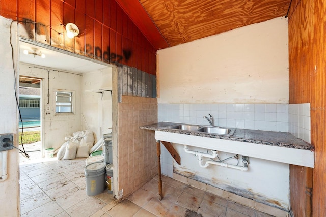 kitchen featuring tile walls, dark stone counters, and a sink