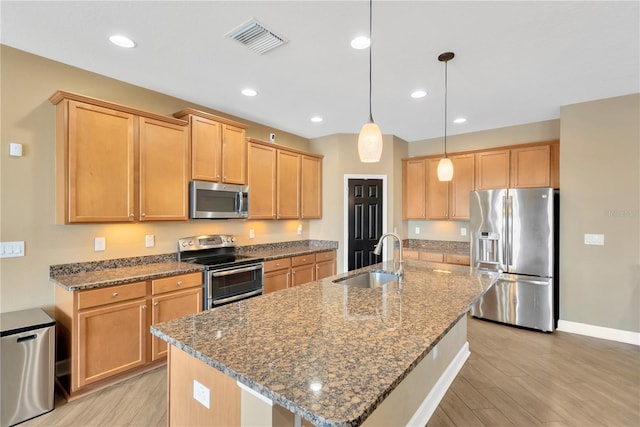 kitchen featuring light wood finished floors, stainless steel appliances, visible vents, a sink, and an island with sink