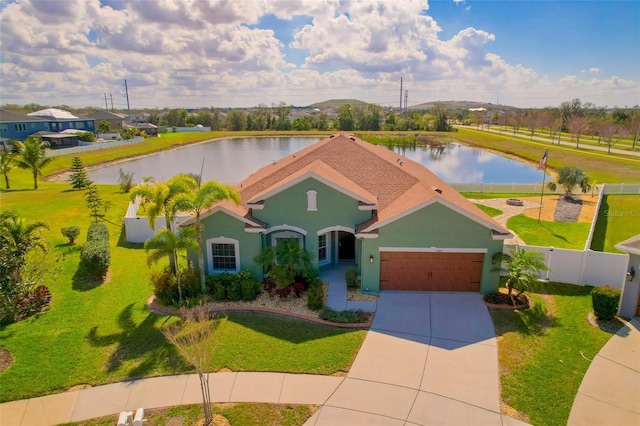 view of front of house featuring an attached garage, a water view, fence, driveway, and stucco siding