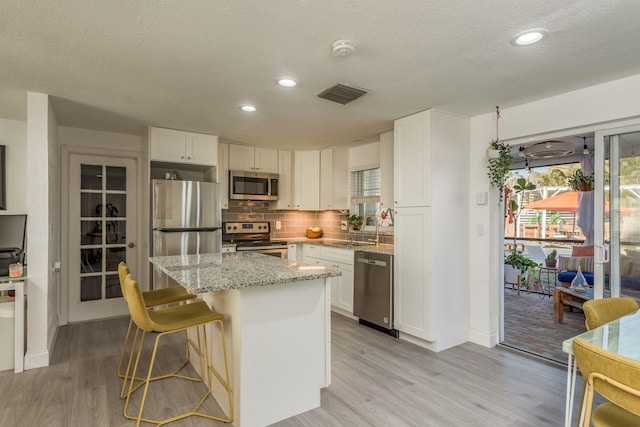 kitchen with stainless steel appliances, light stone counters, light hardwood / wood-style floors, white cabinets, and a kitchen island