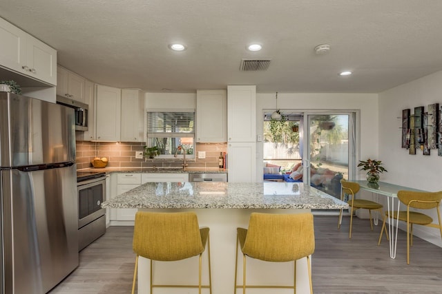 kitchen with a breakfast bar, white cabinetry, a center island, appliances with stainless steel finishes, and light stone countertops