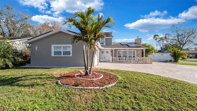 view of front of property with stucco siding, fence, decorative driveway, roof mounted solar panels, and a front yard