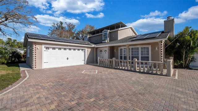 view of front of home featuring decorative driveway, a chimney, stucco siding, roof mounted solar panels, and a garage