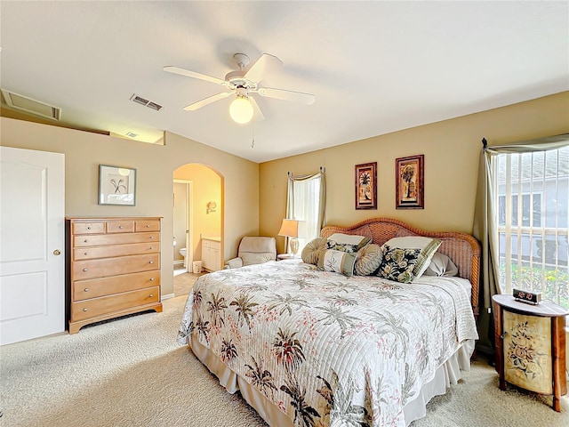 bedroom with multiple windows, connected bathroom, light colored carpet, and ceiling fan