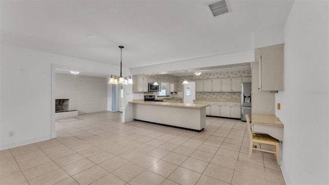 kitchen with white cabinetry, hanging light fixtures, kitchen peninsula, stainless steel appliances, and a fireplace