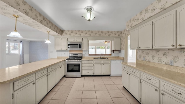 kitchen with sink, light tile patterned floors, appliances with stainless steel finishes, decorative light fixtures, and kitchen peninsula