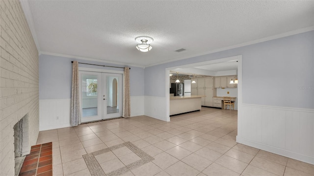 tiled spare room featuring a brick fireplace, ornamental molding, french doors, and a textured ceiling