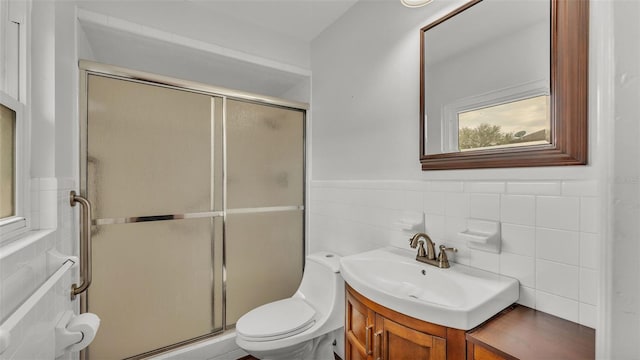 bathroom featuring toilet, tile walls, vanity, and a shower with shower door