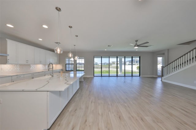 kitchen with baseboards, white cabinets, light wood-style flooring, backsplash, and a sink