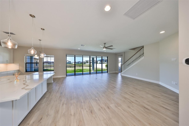 unfurnished living room featuring stairs, light wood finished floors, visible vents, and baseboards