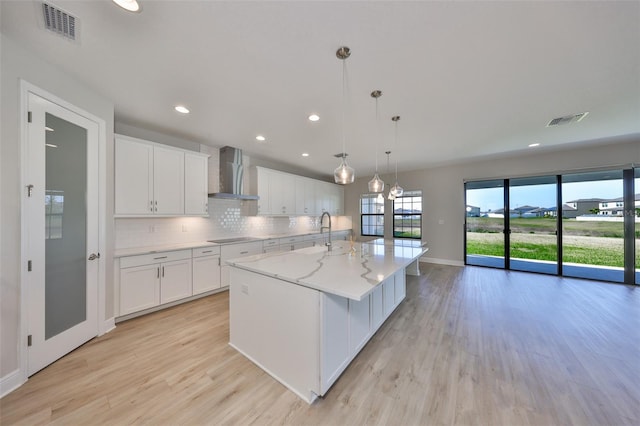 kitchen featuring wall chimney exhaust hood, backsplash, visible vents, and white cabinets