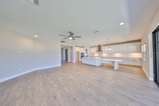 kitchen with light wood finished floors, wall chimney range hood, visible vents, and white cabinets