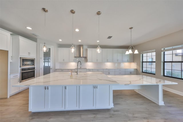 kitchen with white cabinetry, appliances with stainless steel finishes, decorative backsplash, wall chimney exhaust hood, and a large island with sink