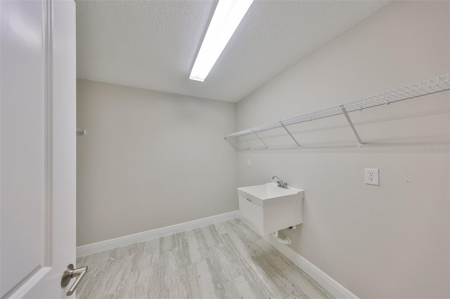 laundry room featuring a textured ceiling, light wood-type flooring, a sink, and baseboards