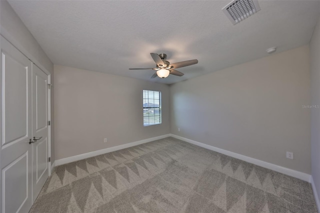 spare room featuring light carpet, a textured ceiling, visible vents, and baseboards