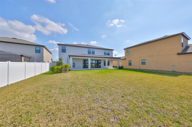 back of property with stucco siding, fence, and a yard