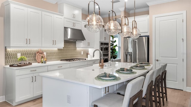 kitchen featuring appliances with stainless steel finishes, a kitchen island with sink, white cabinets, and decorative light fixtures