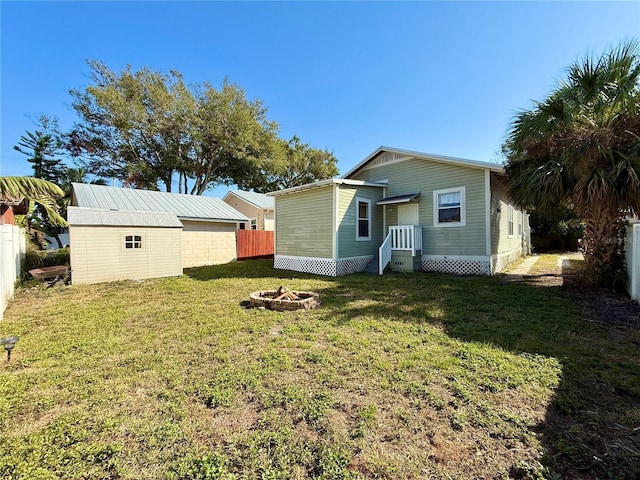 rear view of property with an outdoor fire pit, a shed, and a lawn