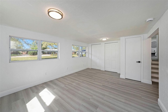 interior space featuring a textured ceiling, wood finished floors, two closets, and baseboards