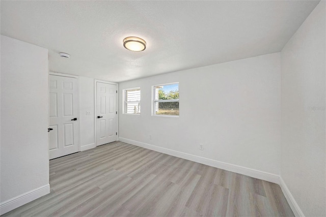 spare room with light wood-style floors, a textured ceiling, and baseboards