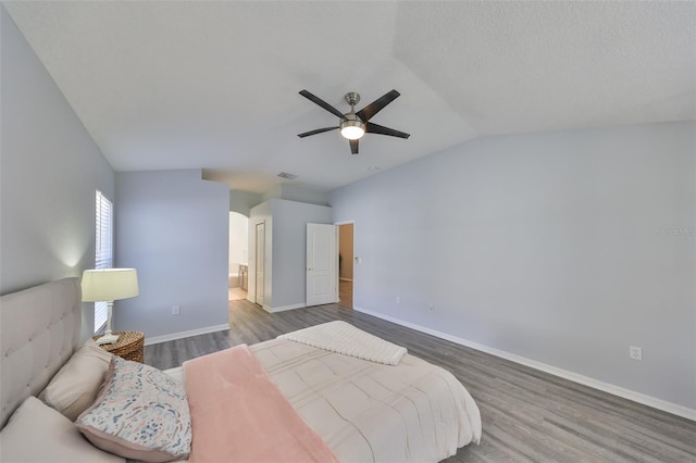 bedroom featuring ensuite bath, vaulted ceiling, a textured ceiling, dark hardwood / wood-style floors, and ceiling fan